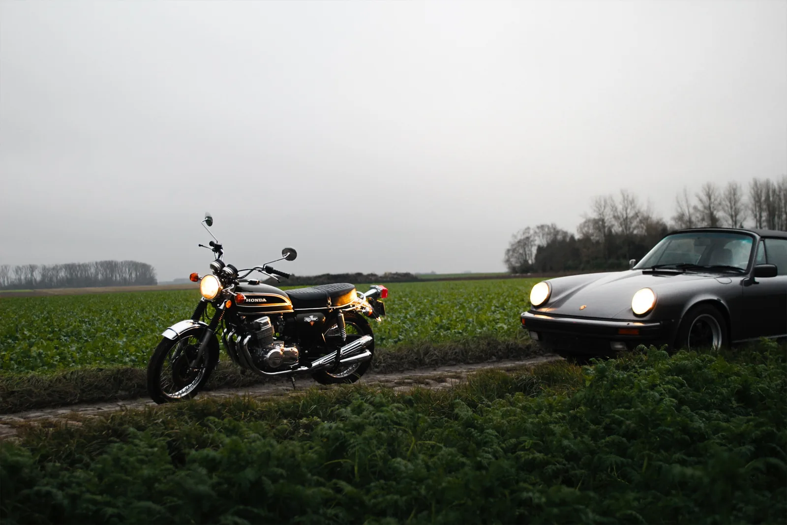 A Honda CB750 and a Porsche 911 side by side in a field at dusk